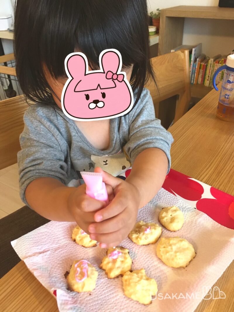 子どもが焼いたクッキーにピンク色のアイシングをしている様子